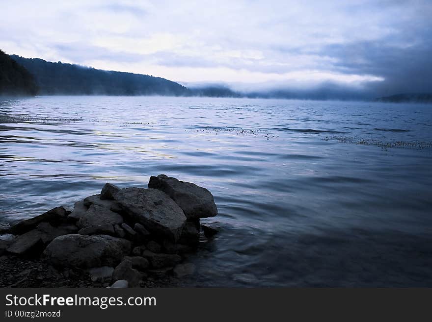 Beautiful water landscape with a fog above water & stones on a foreground. Image in blue, cold tone. Beautiful water landscape with a fog above water & stones on a foreground. Image in blue, cold tone.