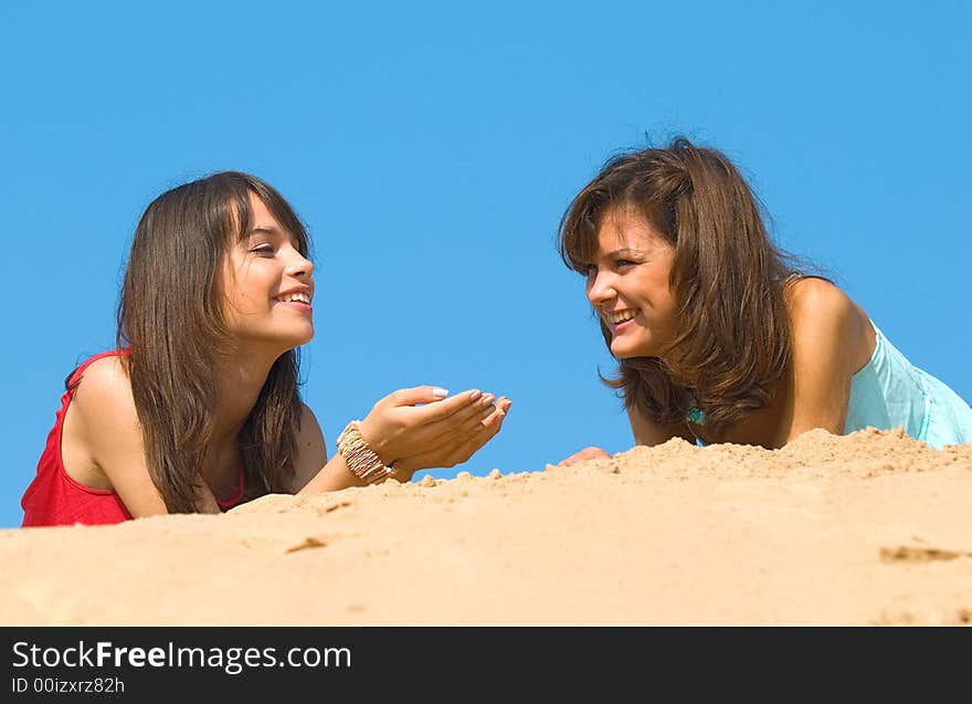 Two happy girlfriends talk on sand under the sun