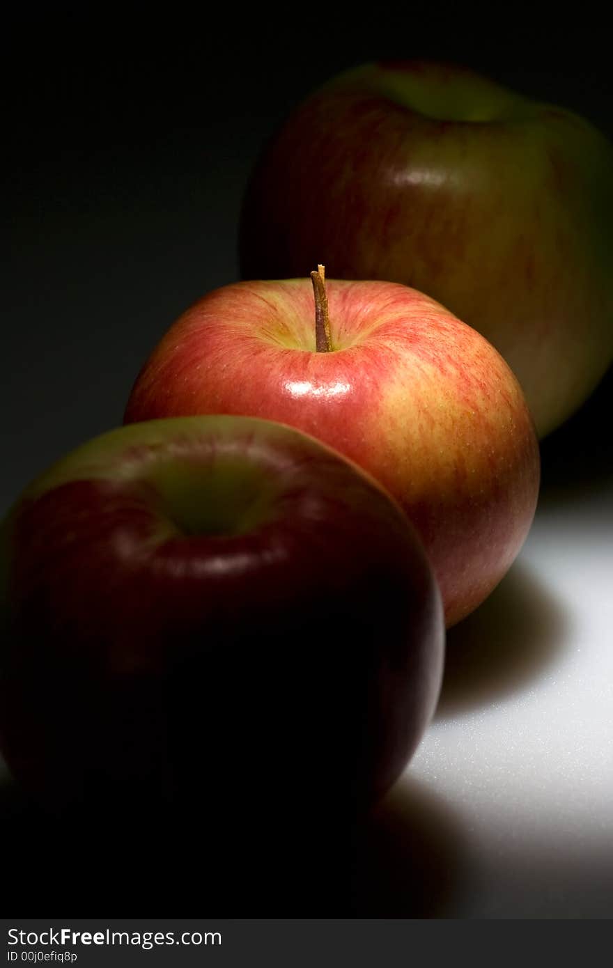 Three red apples in the dark, middle one highlighted.