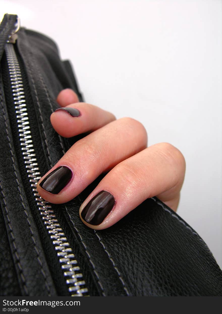 Woman's hand holding a leather handbag. Dark fingernails.