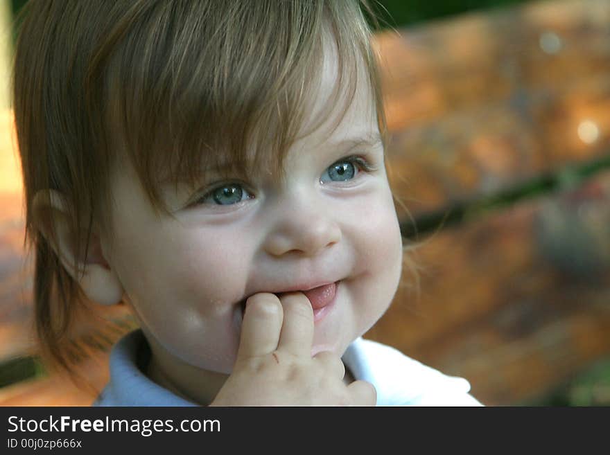 Little smiling girl outdoors with fingers in the mouth