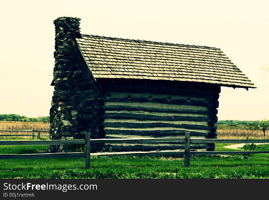 Old log cabin surrounded by wooden fence, cross-processed