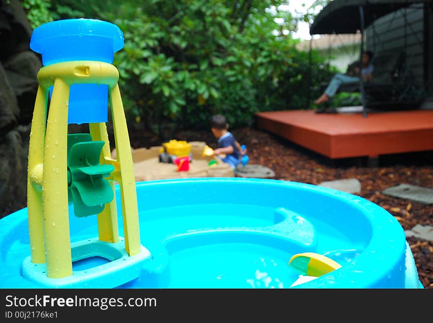 Child Playing in a Sandbox while mother overlooks from a swing