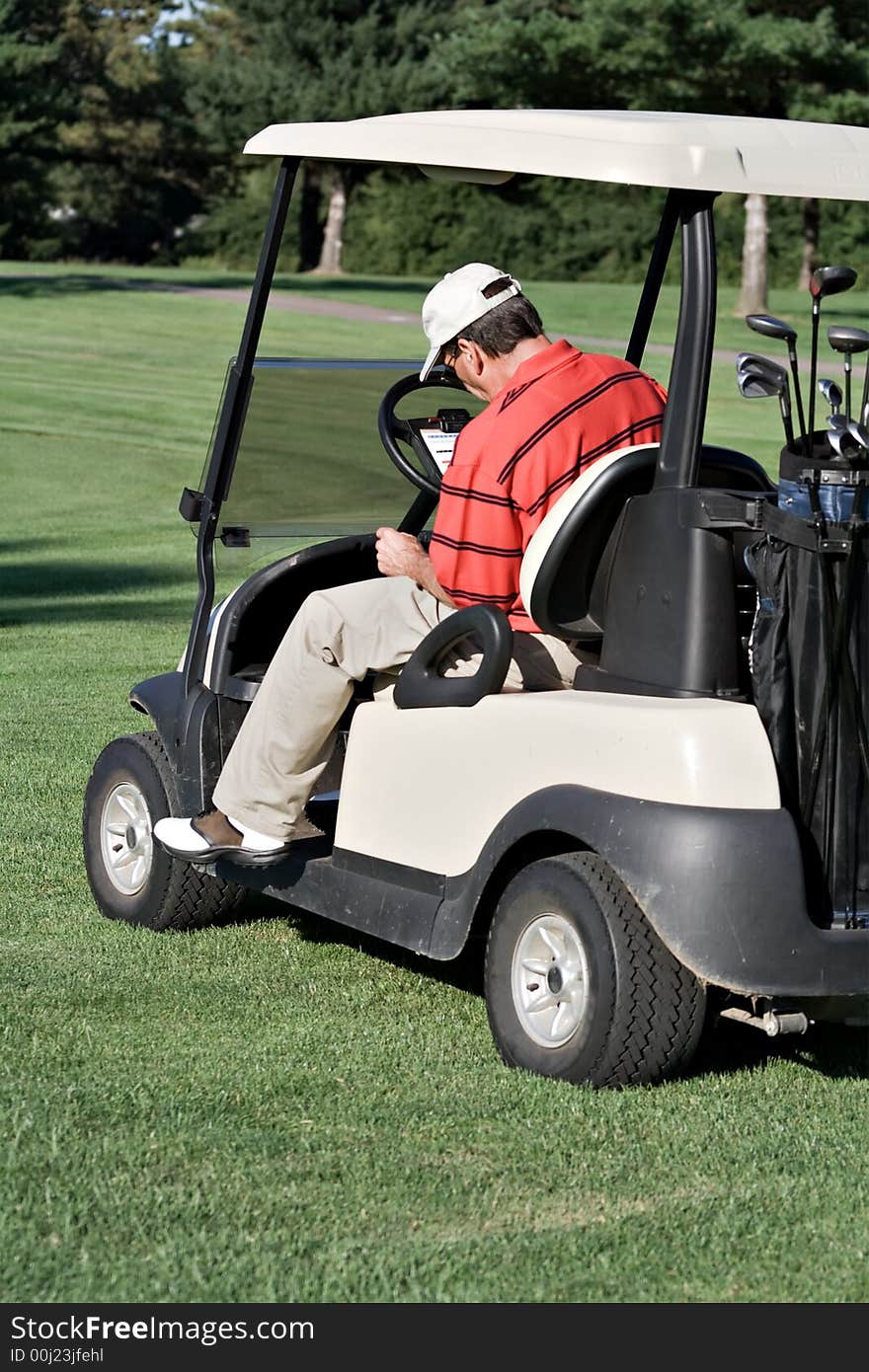 Male golfer sits in cart records his score on score card. Male golfer sits in cart records his score on score card.