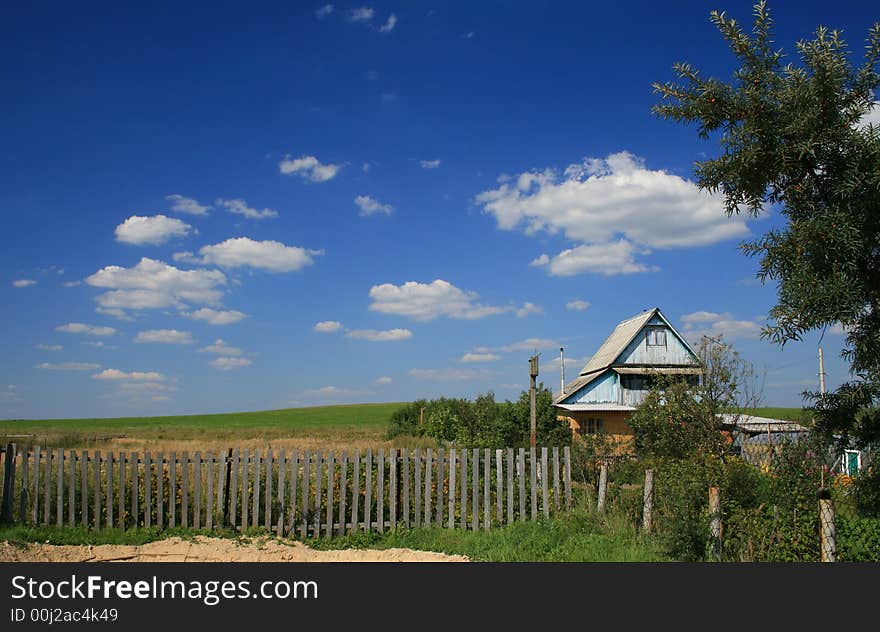 The village house and the green field landscape and blue sky with clouds as a background.