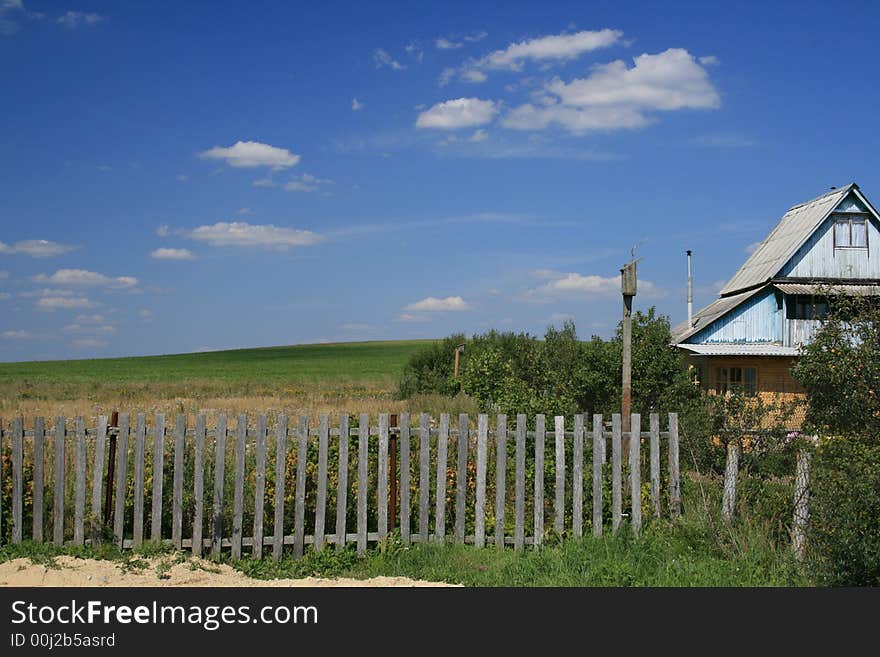 The village house and the green field landscape and blue sky with clouds as a background.