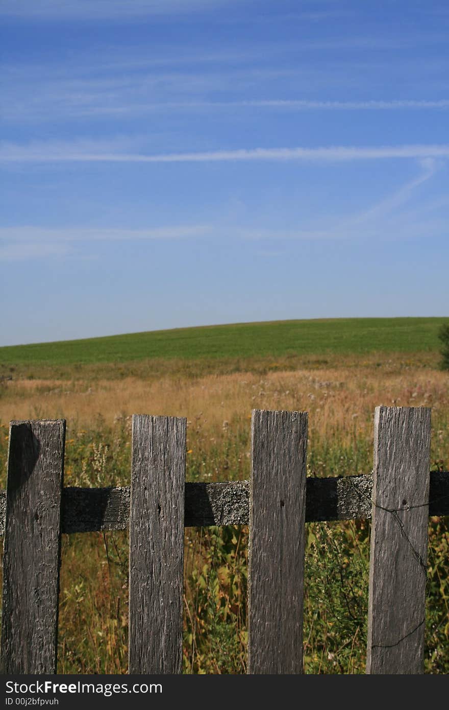 The village fence and the green field and blue sky as a background.