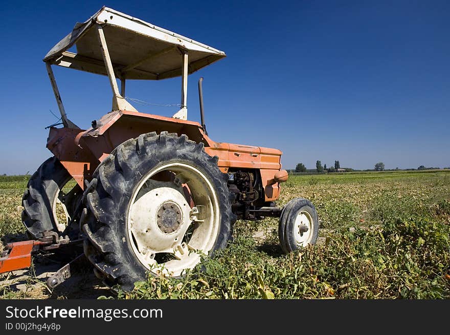 An old orange farm tractor in a cultivated land in countryside. An old orange farm tractor in a cultivated land in countryside