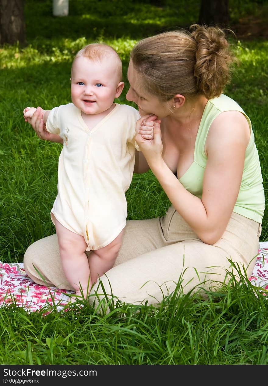 Mother supports the child stand on a green grass. Mother supports the child stand on a green grass