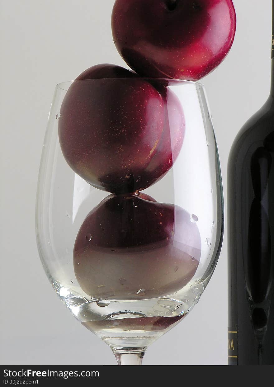 Plums inside a cup and a bottle of wine. Plums inside a cup and a bottle of wine