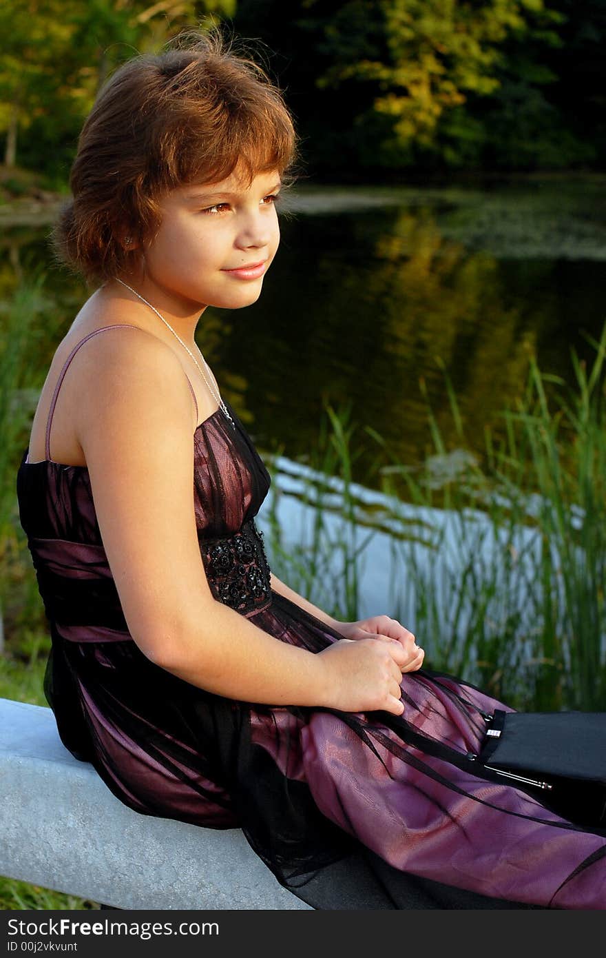 Elementary girl in formal wear gazing into the distance from a pond in late afternoon. Elementary girl in formal wear gazing into the distance from a pond in late afternoon.