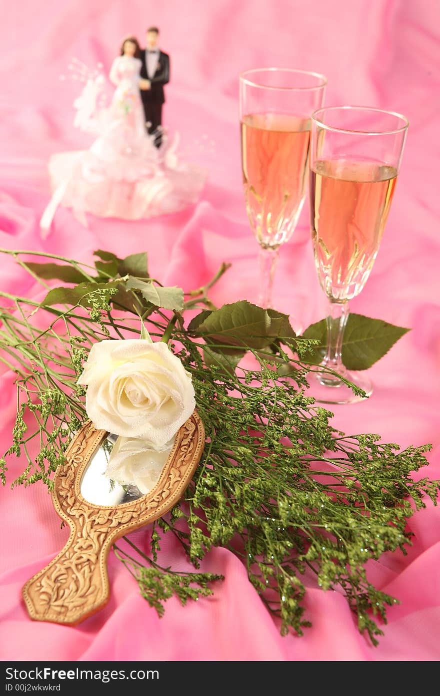 A photo of wedding cake dolls, rose and glasses over pink