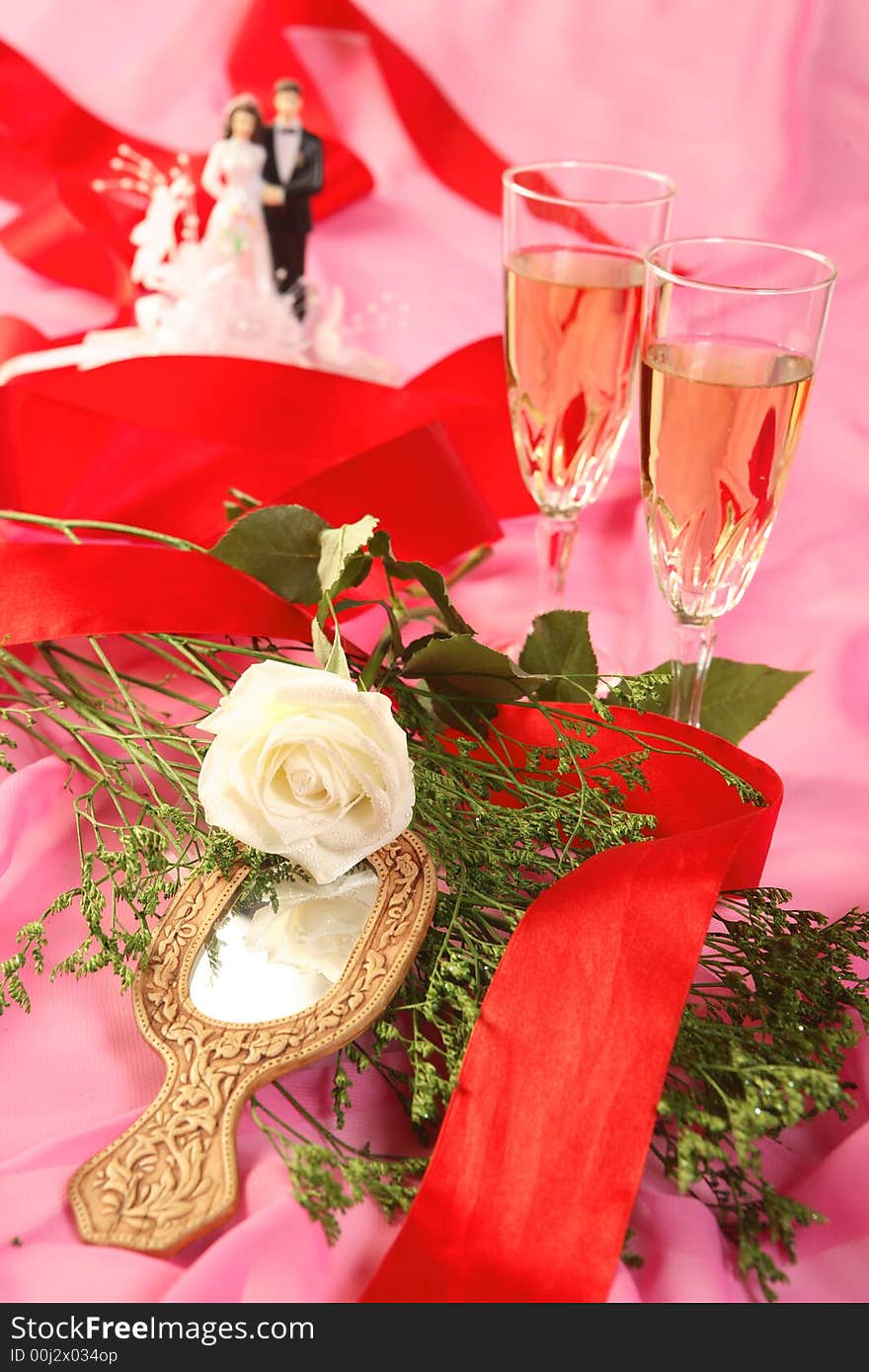 A photo of wedding cake dolls, rose and glasses over pink