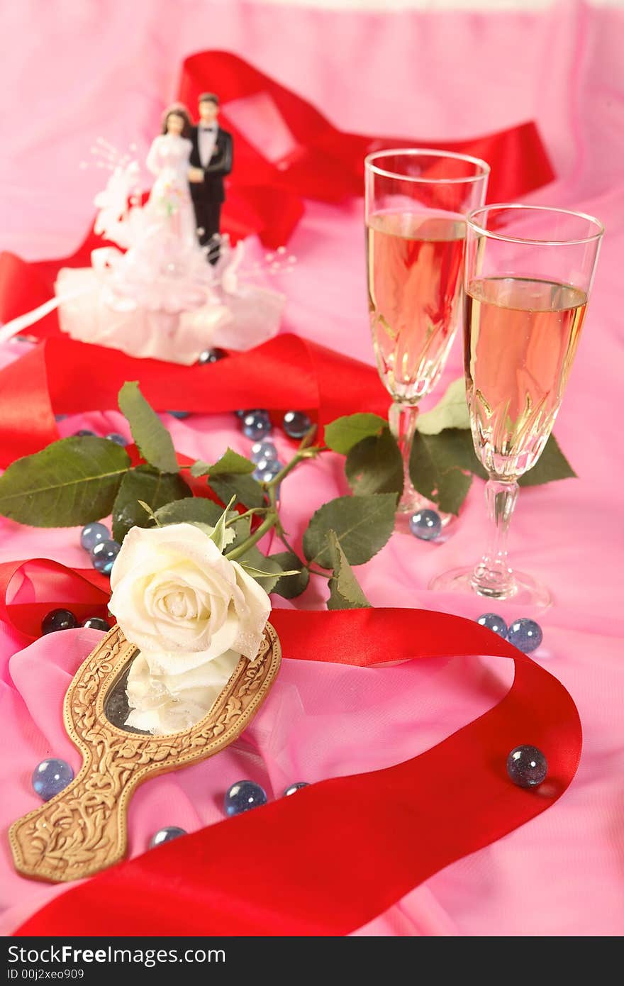 A photo of wedding cake dolls, rose and glasses over pink