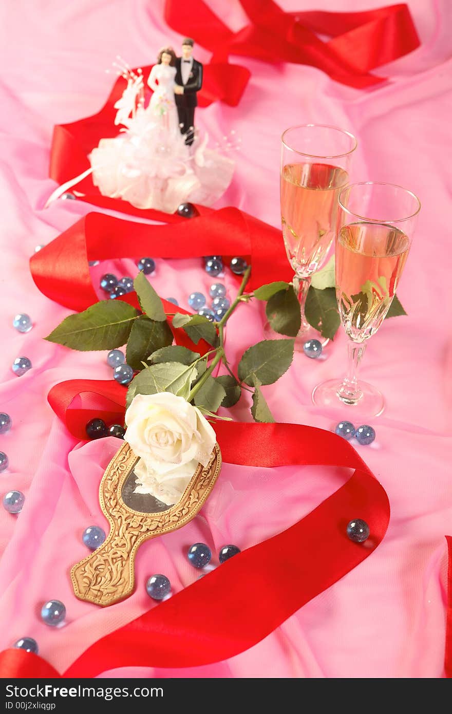 A photo of wedding cake dolls, rose and glasses over pink