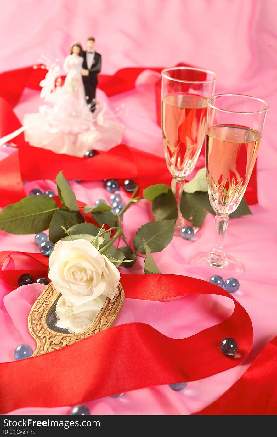 A photo of wedding cake dolls, rose and glasses over pink