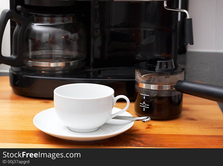 Closeup of white cup with coffee machine in the background and pot full of coffee next to it. Closeup of white cup with coffee machine in the background and pot full of coffee next to it