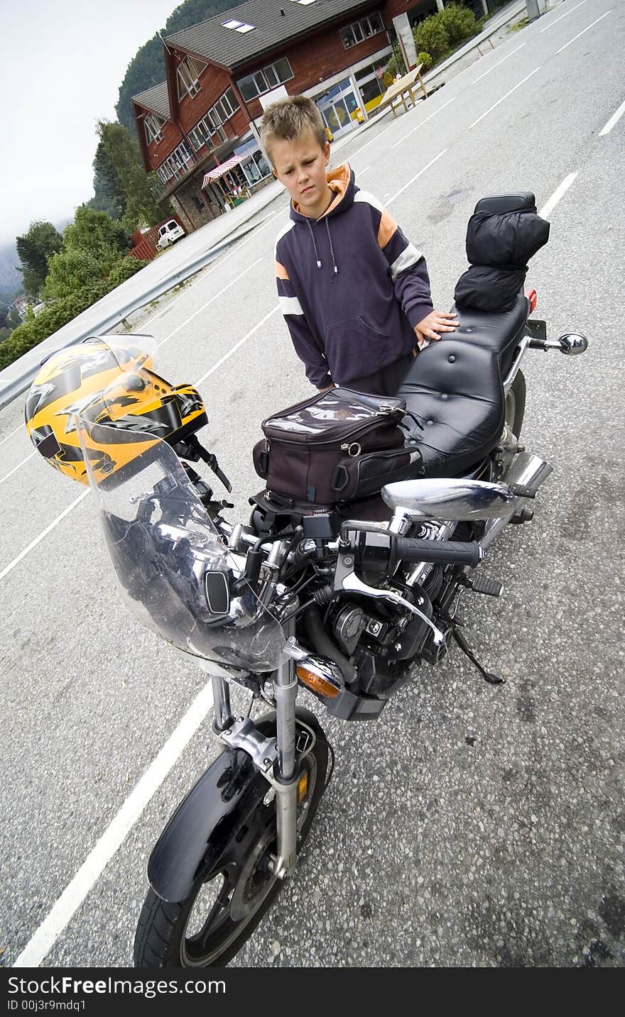 A boy standing next to a motorbike, looking at it with admiration. Wide angle view. A boy standing next to a motorbike, looking at it with admiration. Wide angle view.