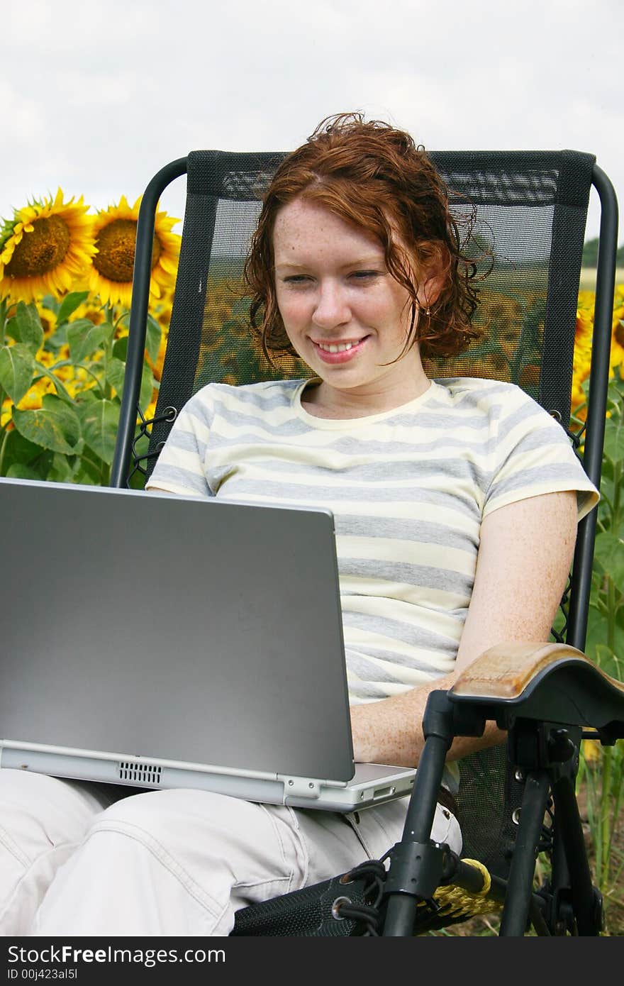 A young lady working on her laptop by a field of sunflowers. A young lady working on her laptop by a field of sunflowers