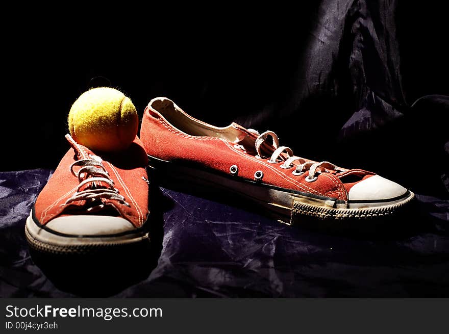 Red old sneakers and tennis ball on the dark blue background