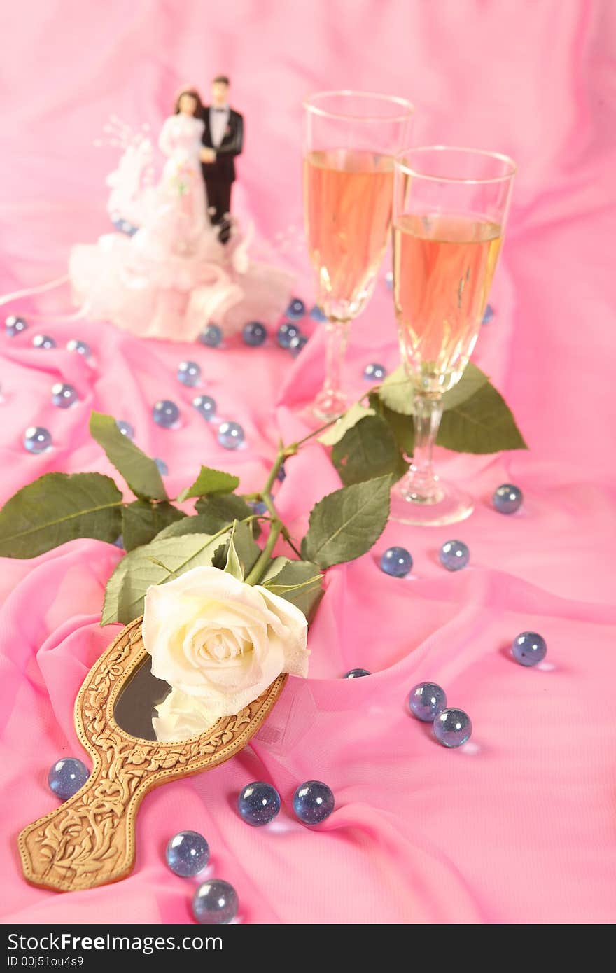 A photo of wedding cake dolls, rose and glasses over pink