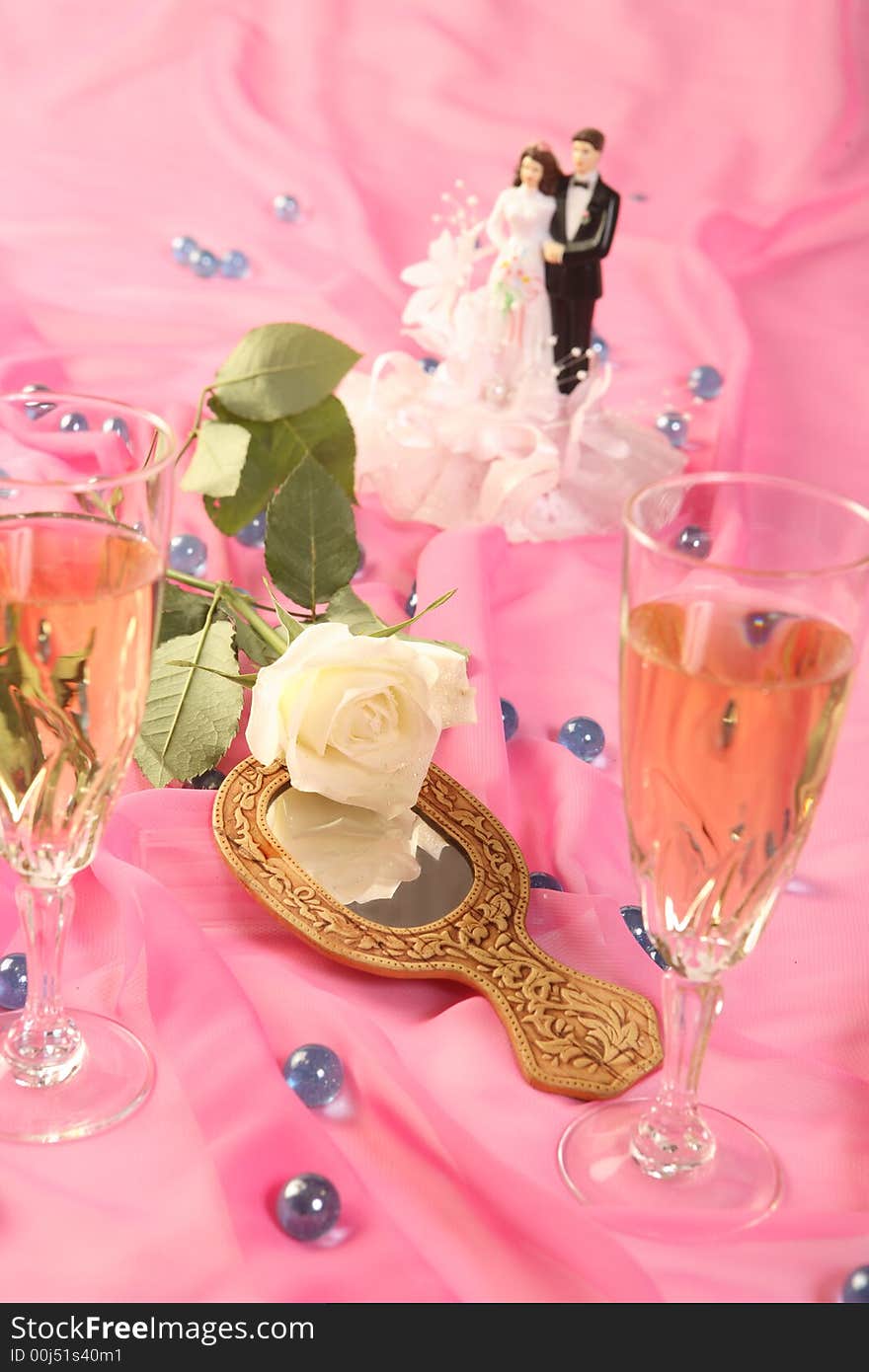 A photo of wedding cake dolls, rose and glasses over pink