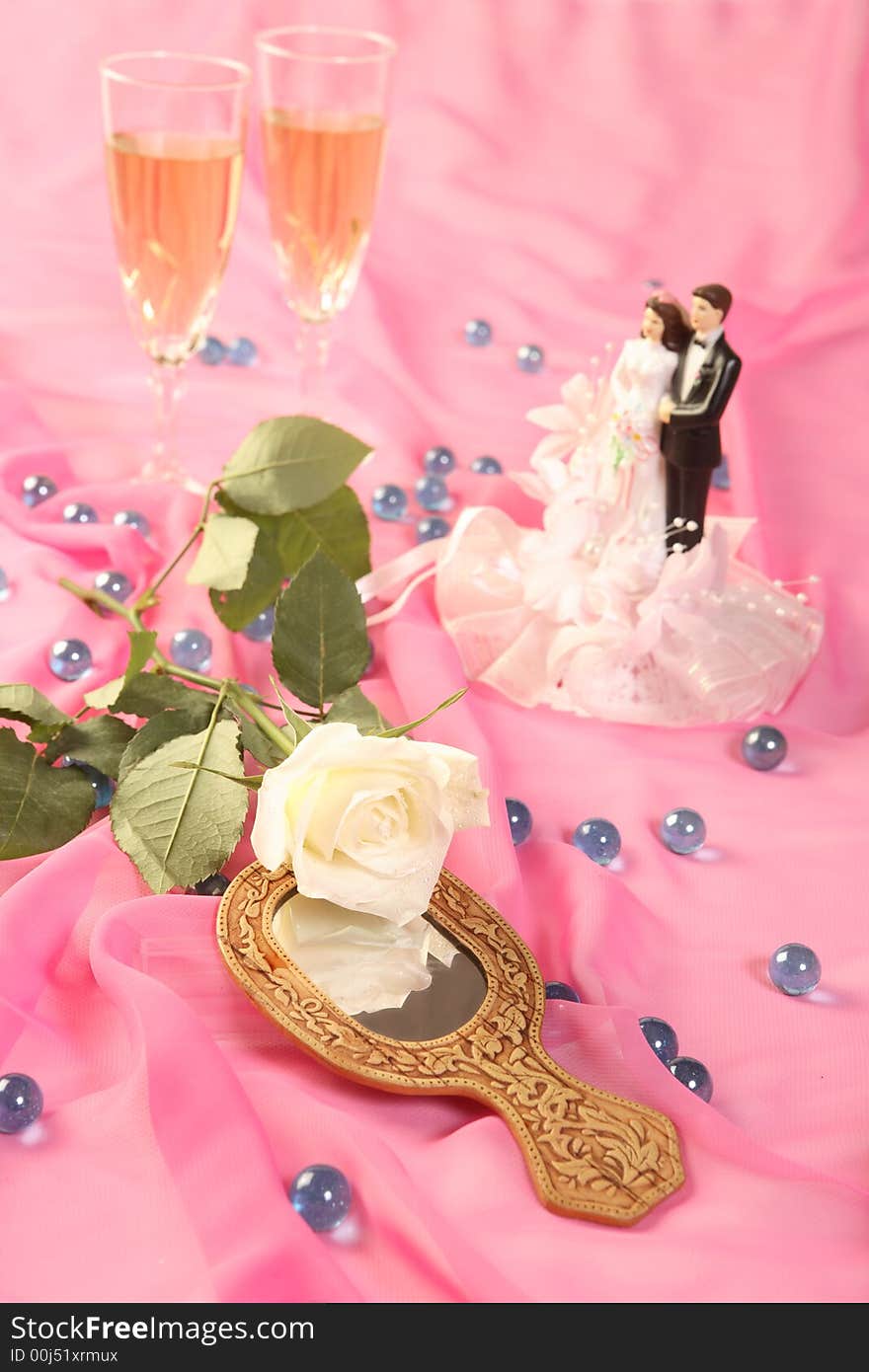 A photo of wedding cake dolls, rose and glasses over pink