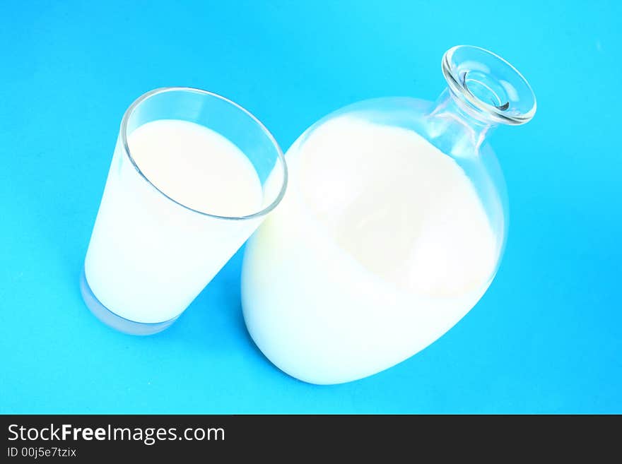 Pouring white milk against blue background and glass