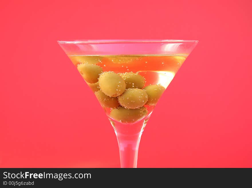 Olive cocktail in a martini glass on a red background. Olive cocktail in a martini glass on a red background