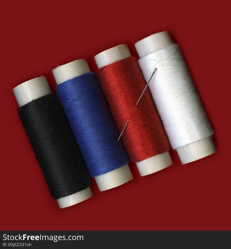 Fourth colorful spools of thread with a needle on red background