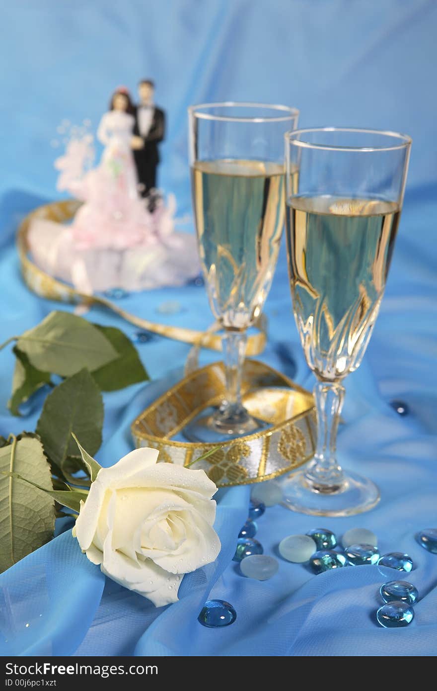 A photo of wedding cake dolls, rose and glasses over blue