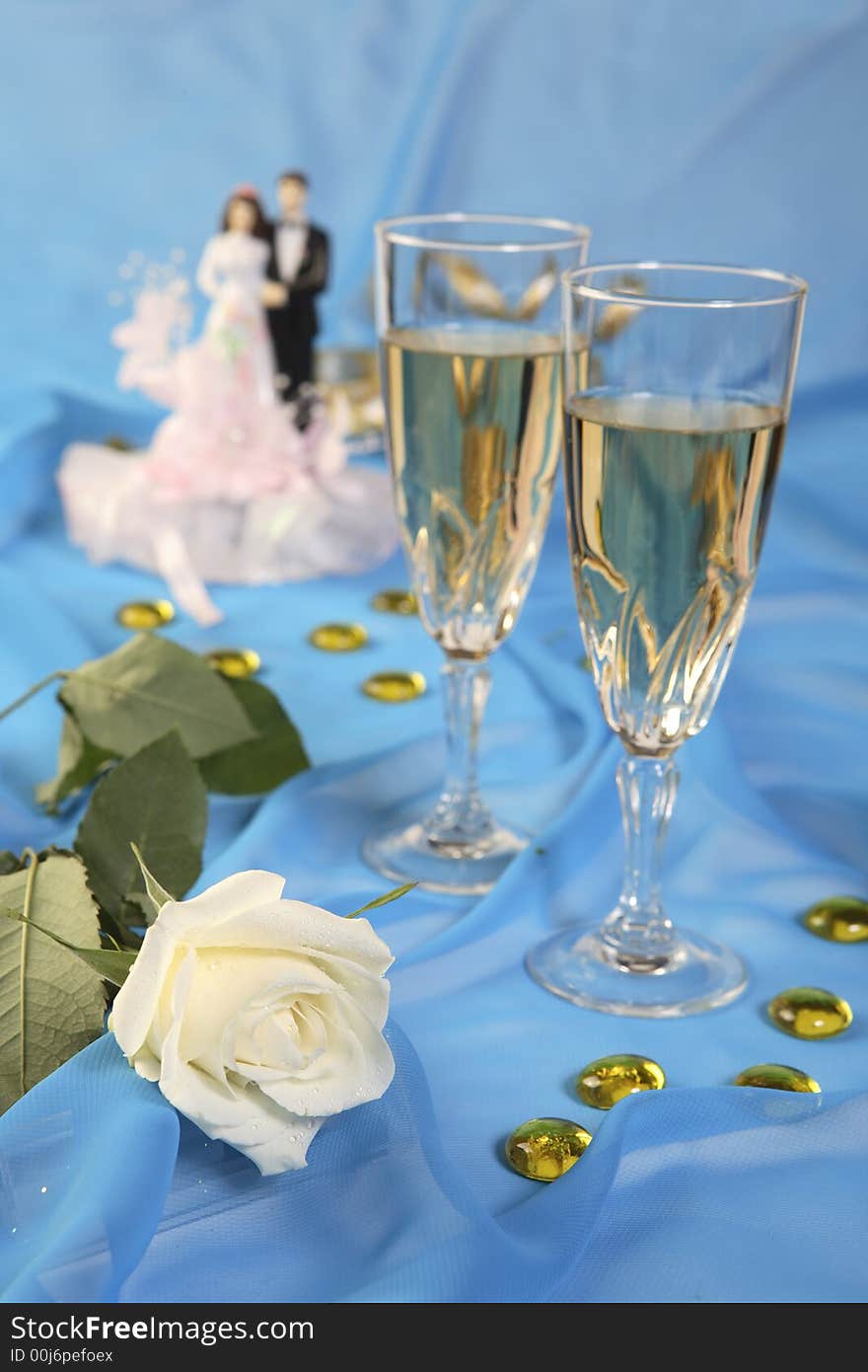 A photo of wedding cake dolls, rose and glasses over blue