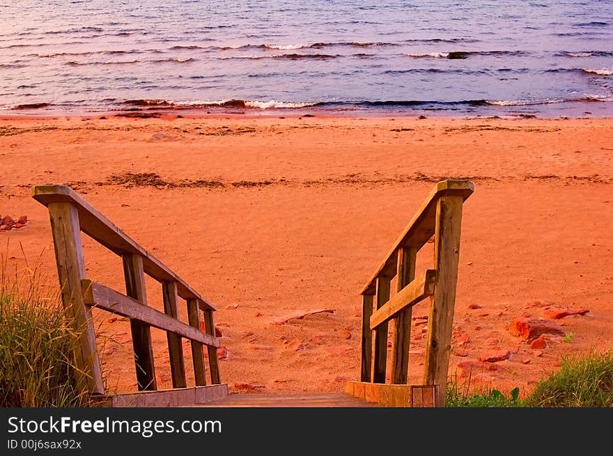 A flight of wooden stairs descending to a red sandy beach in sunset light.