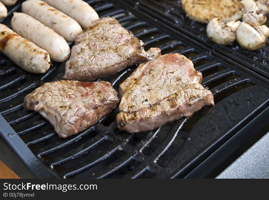 A selection of meats on a gas barbecue, focusing on steak & sausages