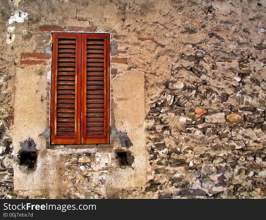 Old window with closed shutters and decayed stone wall