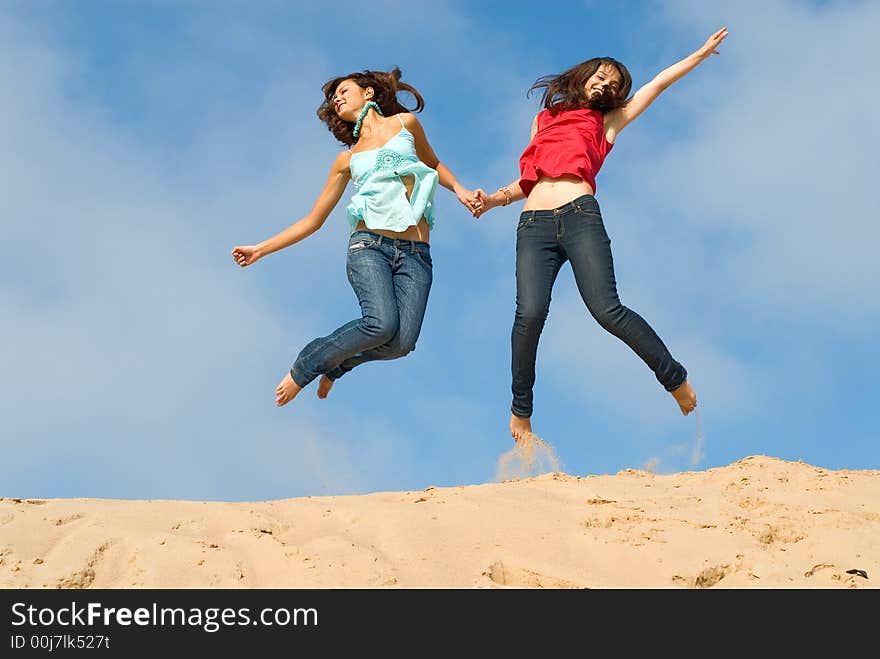 Two girlfriends jump with happiness on sand. Two girlfriends jump with happiness on sand