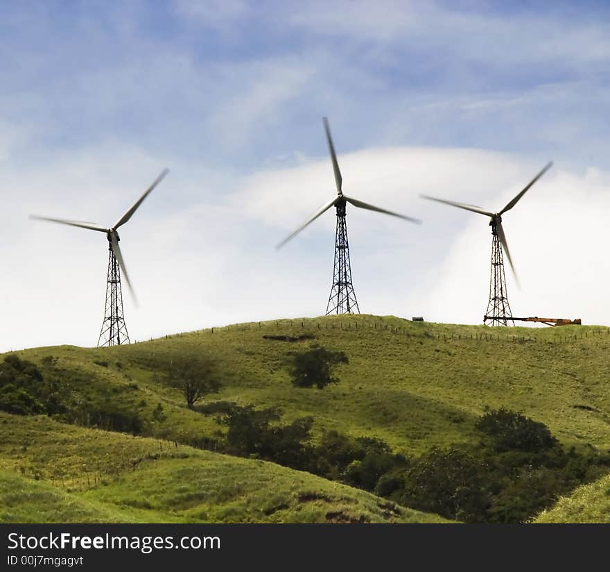 Three windmills harvesting power on a green hilltop. Three windmills harvesting power on a green hilltop.