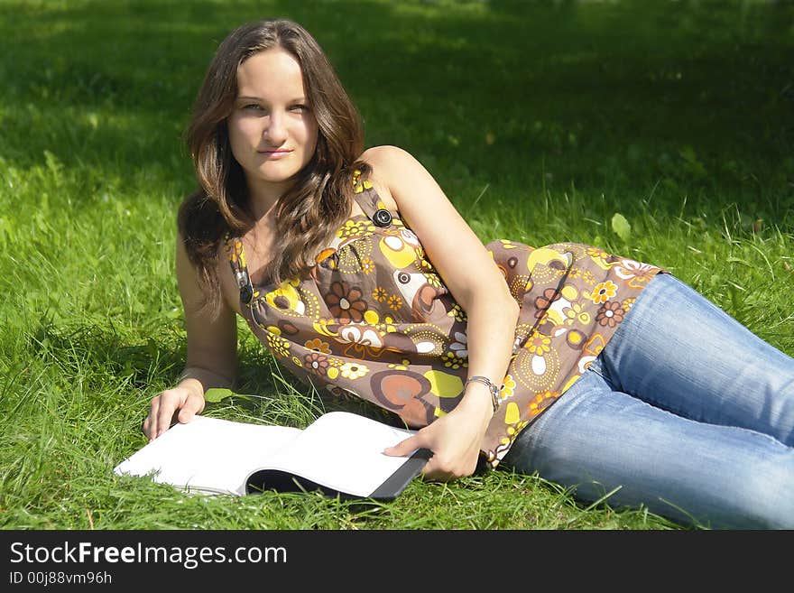 Young brunette girl lying on the grass with an open book. Young brunette girl lying on the grass with an open book