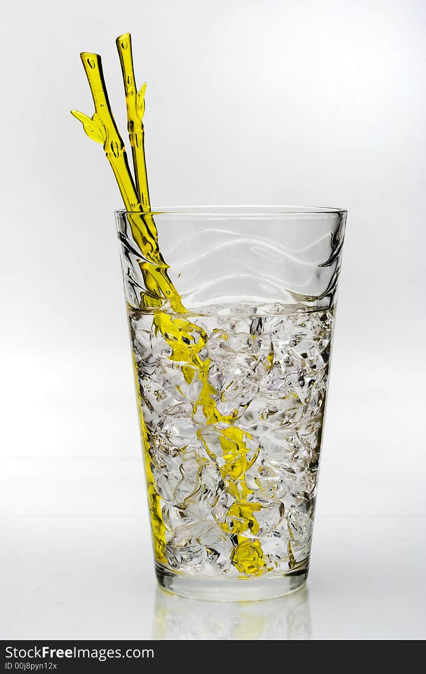 Cold drink with ice and yellow stirring rod isolated on white background