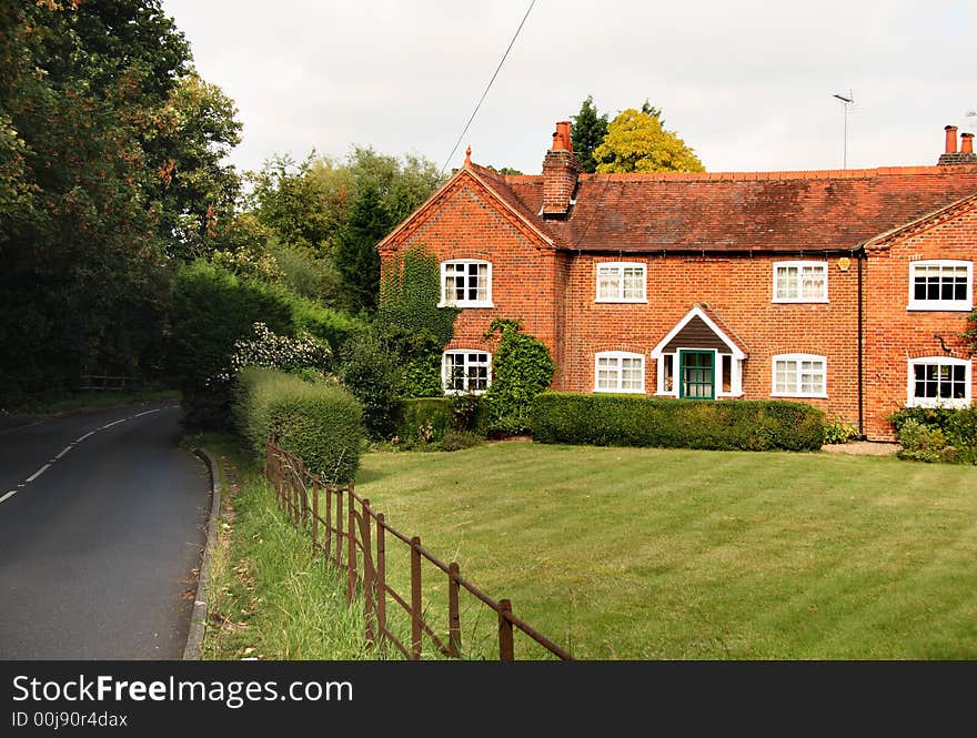 Quaint red brick English Rural Cottage and garden with an iron fence bordering the lawn