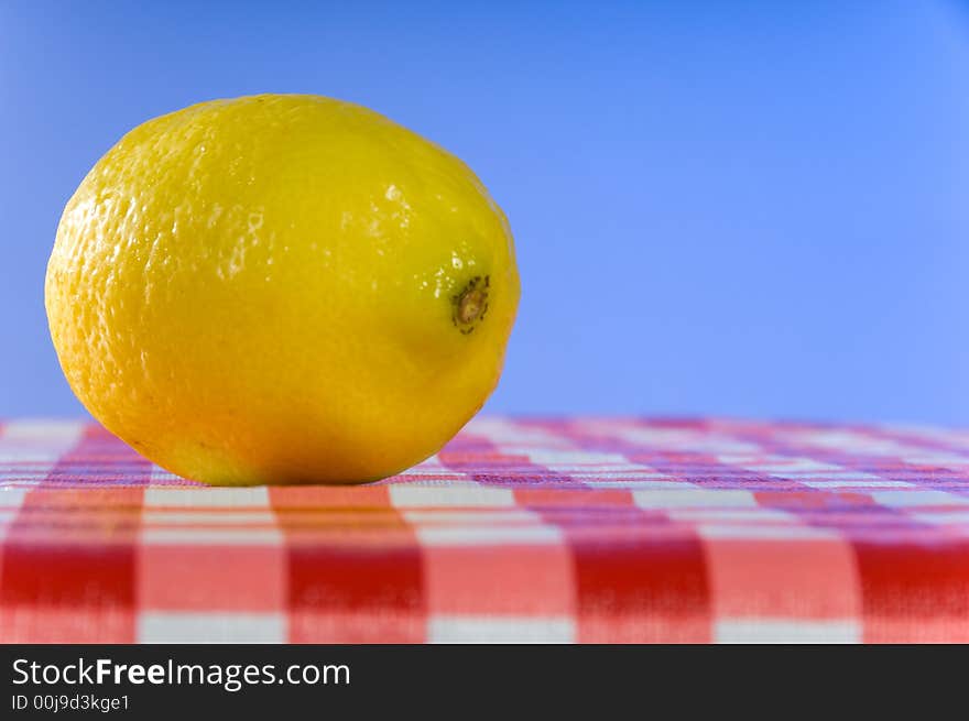 Fresh lemon on gingham tablecloth at picnic against blue sky background. Fresh lemon on gingham tablecloth at picnic against blue sky background