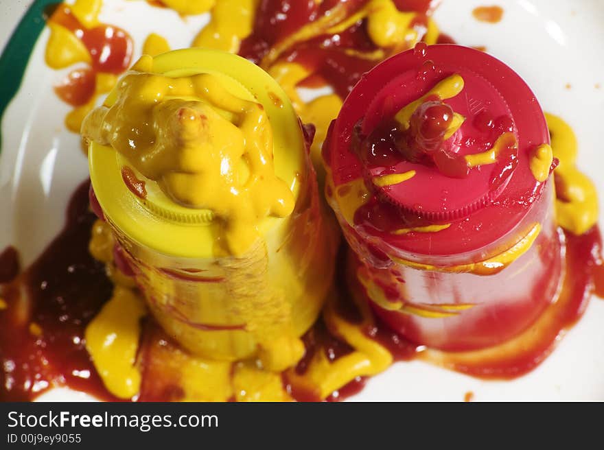 Messy mustard and ketchup squeeze bottles standing up on a plate.