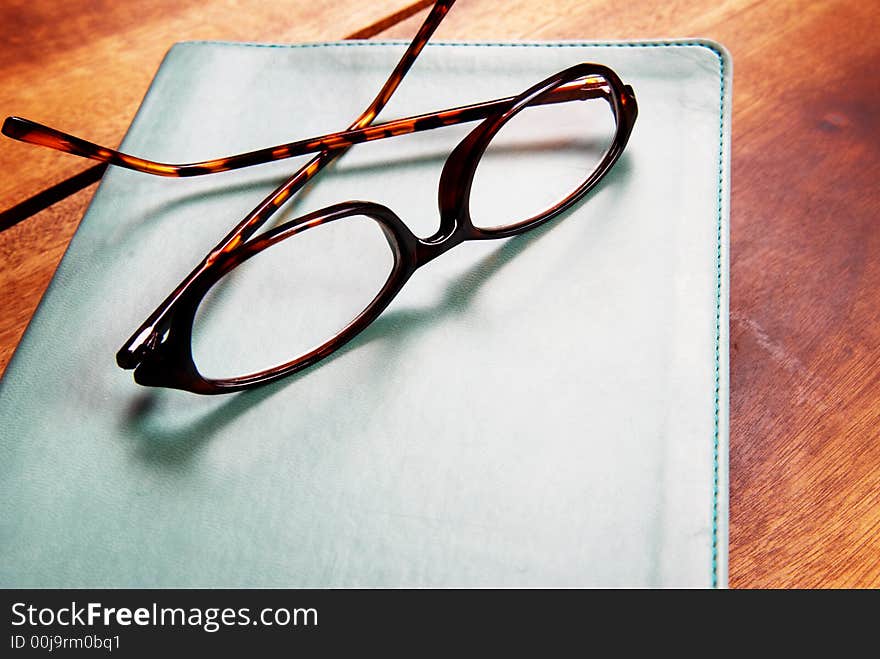 Leopard patern reading glasses lying on a book. Everything is lying on a wood table. Leopard patern reading glasses lying on a book. Everything is lying on a wood table