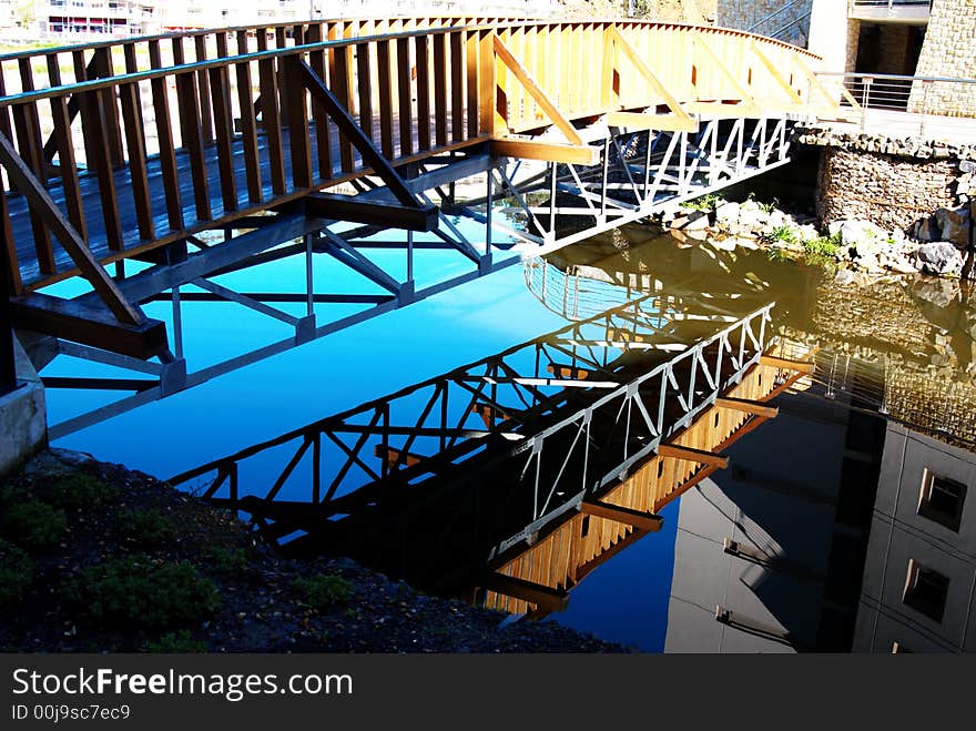 A wooden bridge with steel construction beams over a lake. perfect reflection of the bridge can be seen in the water. A wooden bridge with steel construction beams over a lake. perfect reflection of the bridge can be seen in the water.