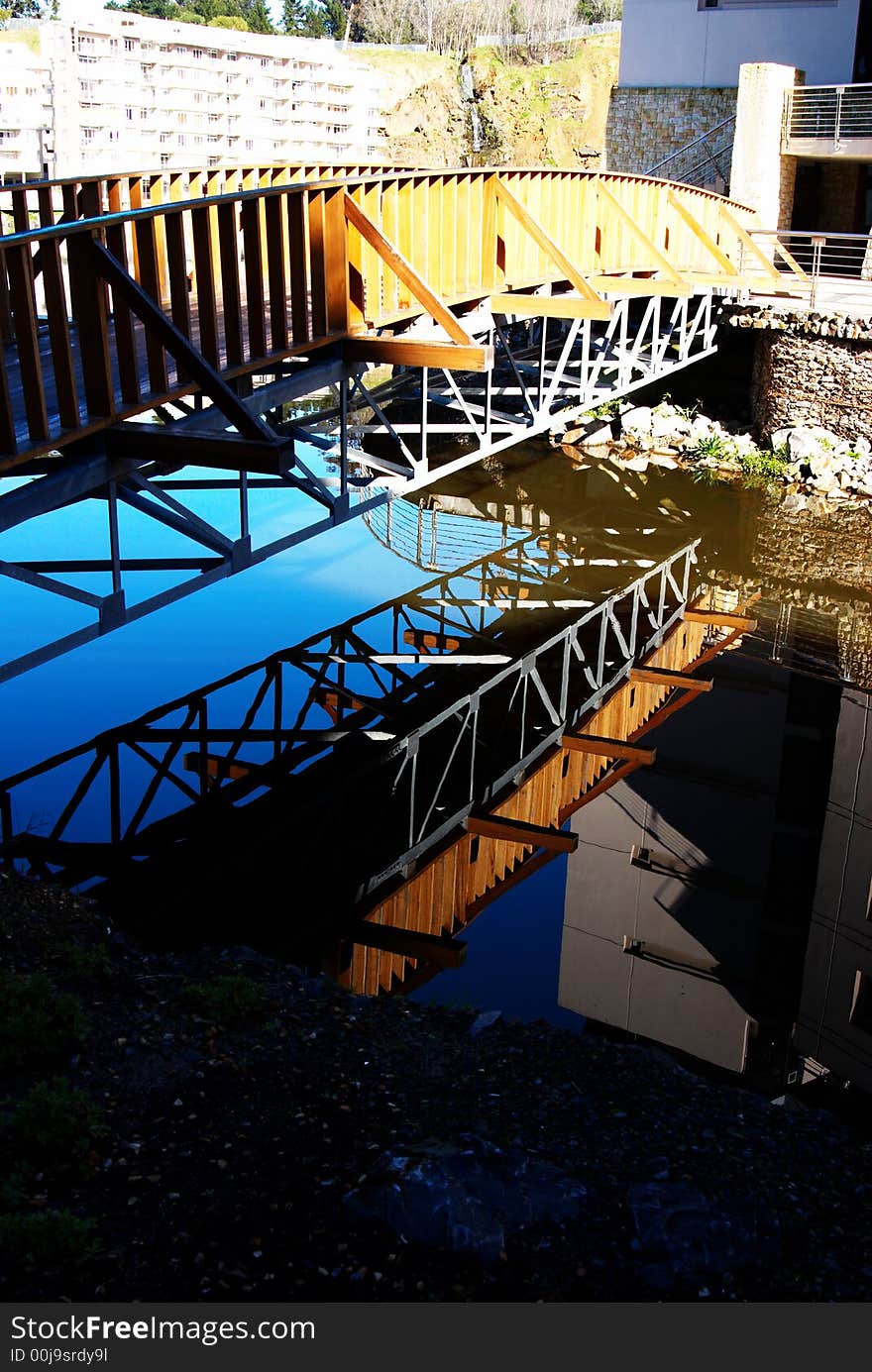 A wooden bridge with steel construction beams over a lake. perfect reflection of the bridge can be seen in the water. A wooden bridge with steel construction beams over a lake. perfect reflection of the bridge can be seen in the water.