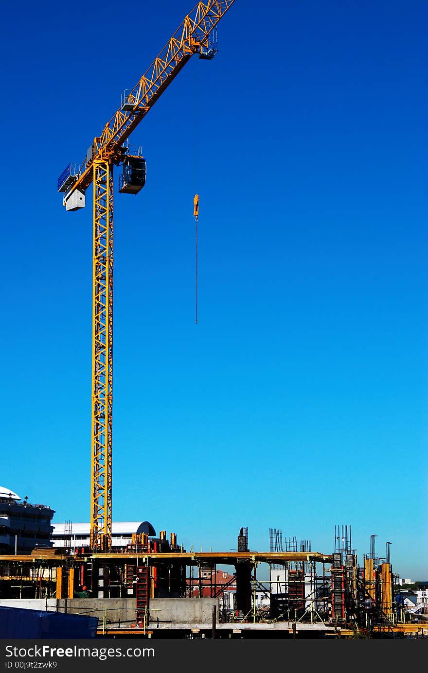 A yellow construction crane on a constuction site with the lifting cable hanging in mid air