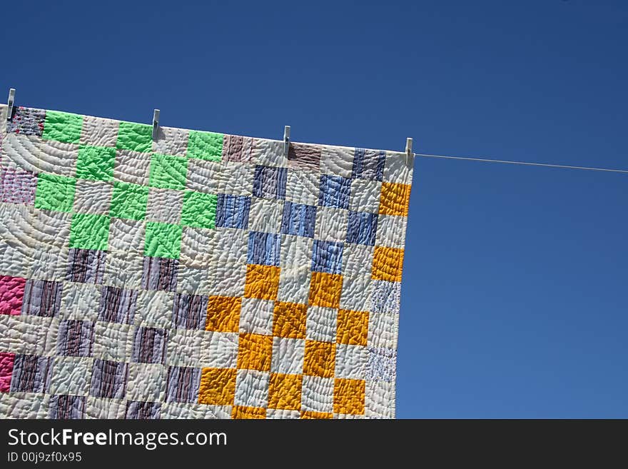 Laundry. Bright patchwork counterpane hanging to dry on a clothes-line.