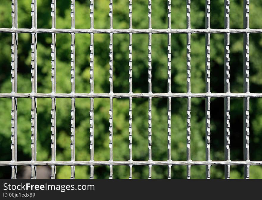 Metal grid with green blurry trees on the background. Metal grid with green blurry trees on the background.