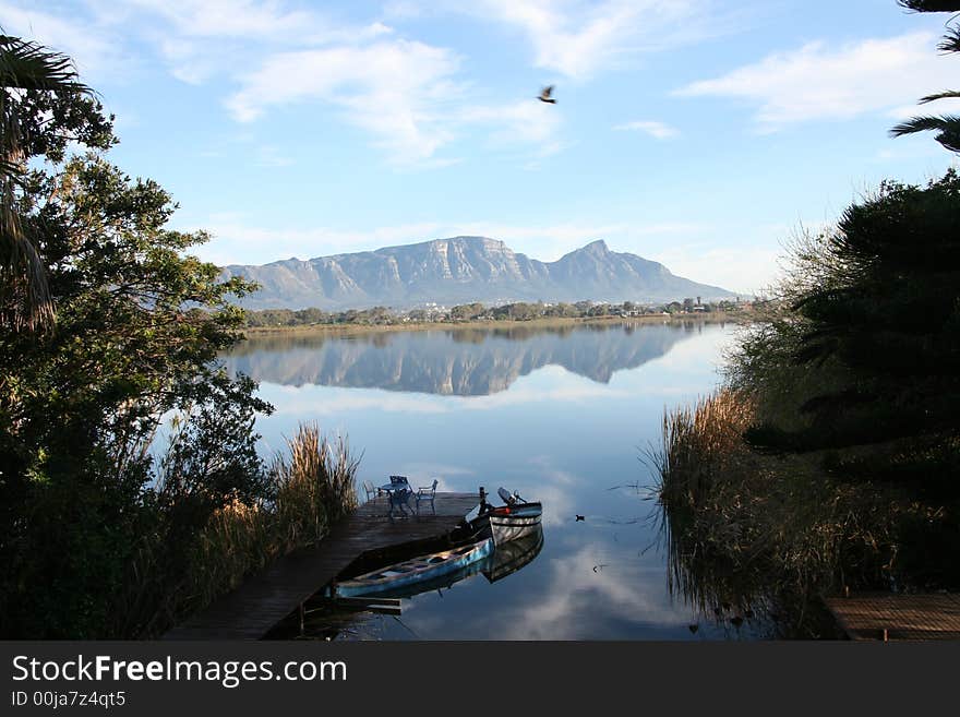 Still, windless day at Zeekoevlei, Cape Town. Reflection of Table Mountain and Devil's Peak with boats in foreground. Still, windless day at Zeekoevlei, Cape Town. Reflection of Table Mountain and Devil's Peak with boats in foreground.