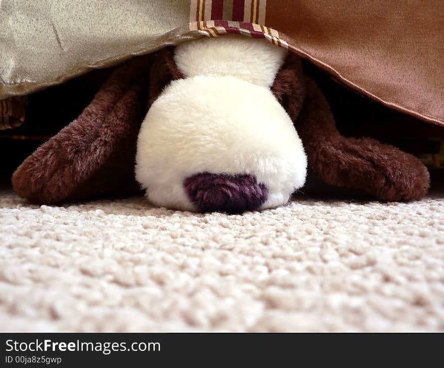 A stuffed toy dog hiding under a bed. A stuffed toy dog hiding under a bed